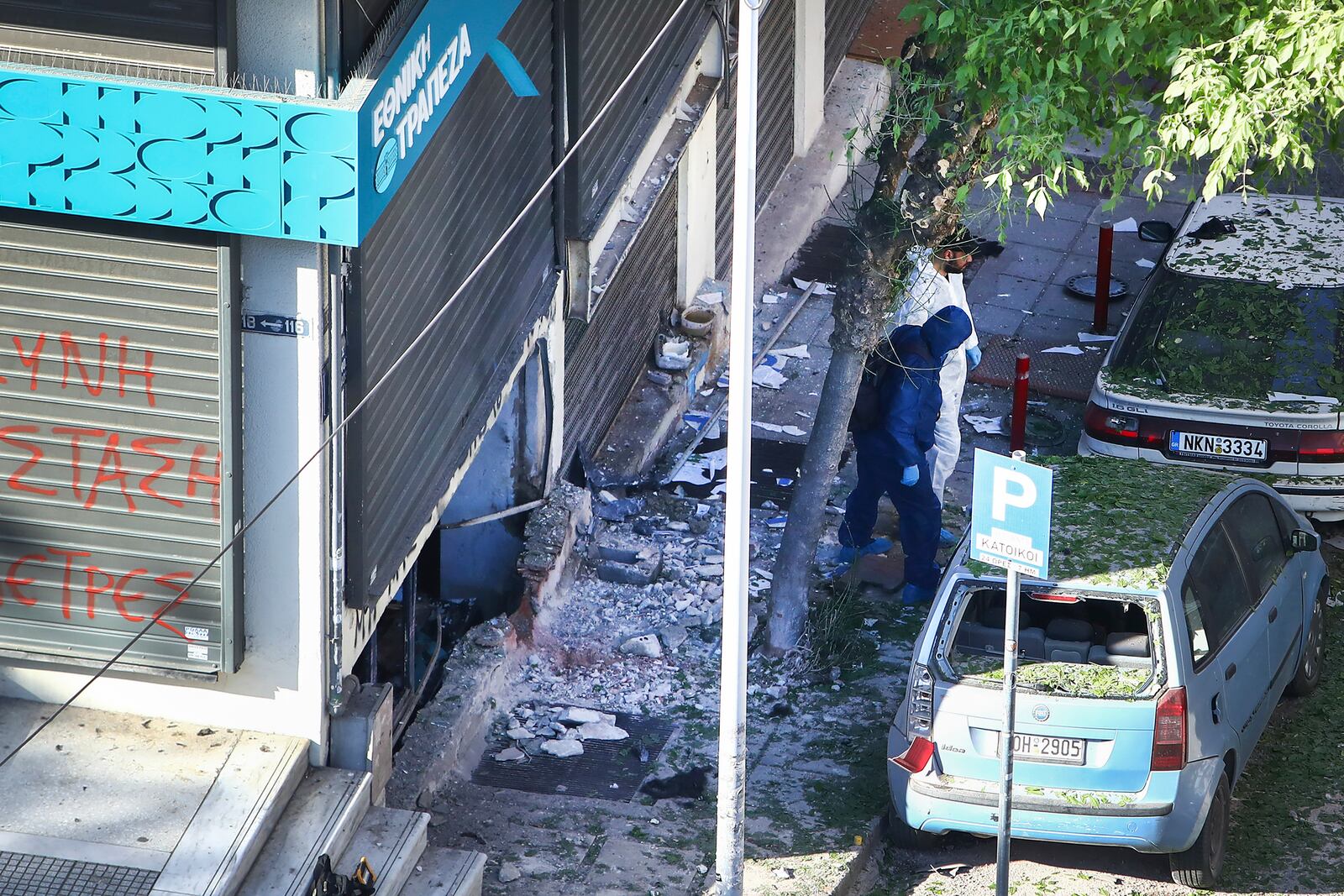 Greek police forensic experts search the area where a 38-year-old woman was killed early Saturday when a bomb she was carrying exploded in her hands outside a bank branch, local police said, in Thessaloniki, northern Greece, May 3, 2025. (AP Photo/Giannis Papanikos)