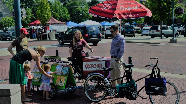 Chuck and Lori Rey with their children, Tripp and Siena, look over the book selection on the Oxford Lane Public Library’s Bike-Mobile. Looking on is Bethany MacMillan with Enjoy Oxford’s Ambassador Bike, along with Chad Wonsik, of the Lane Library. The two bikes are Uptown on Saturday mornings. CONTRIBUTED/BOB RATTERMAN