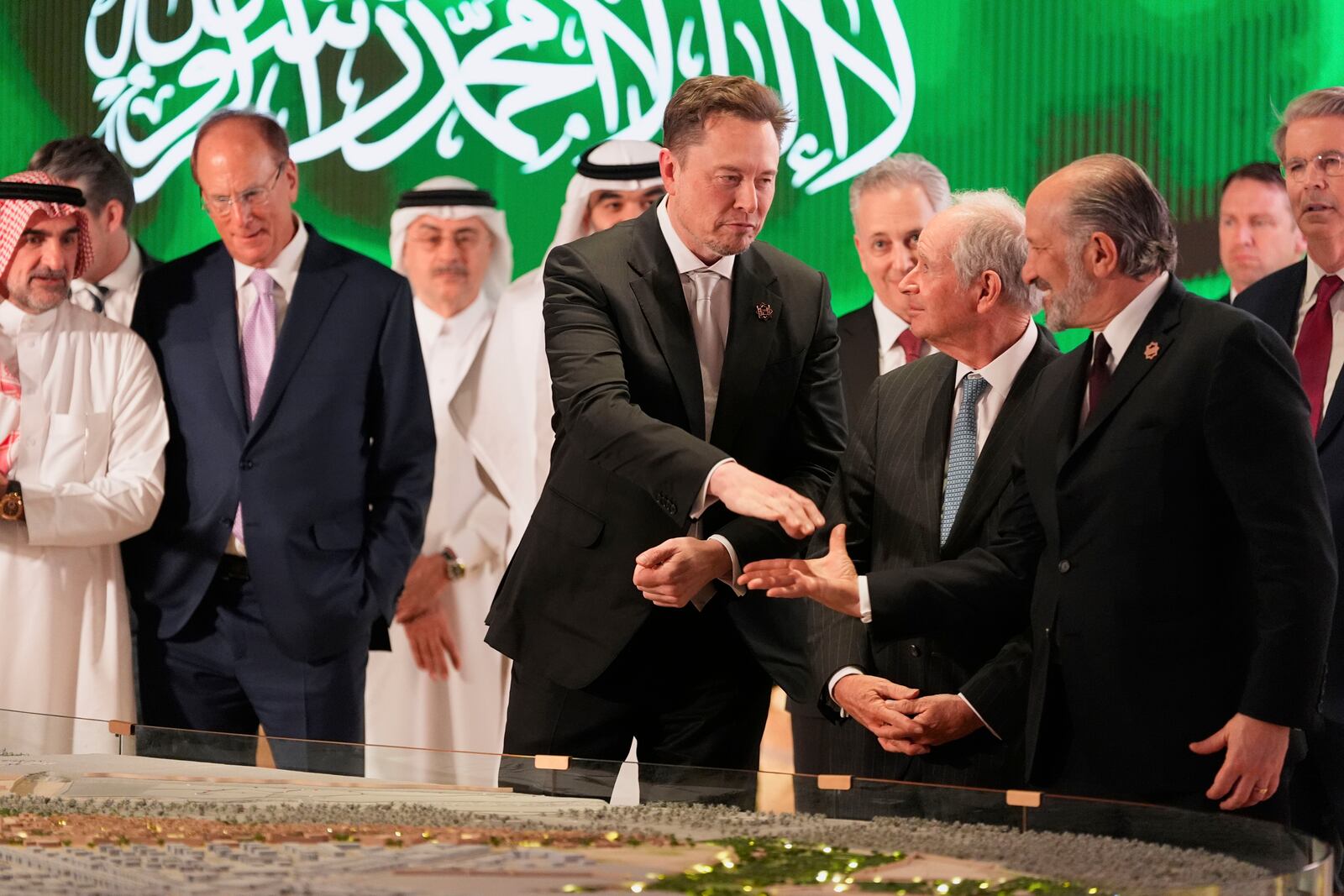 Elon Musk, center, shakes hands with Secretary of Commerce Howard Lutnick, right, as they look at a model of a city under construction, Tuesday, May 13, 2025, in Riyadh, Saudi Arabia. (AP Photo/Alex Brandon)