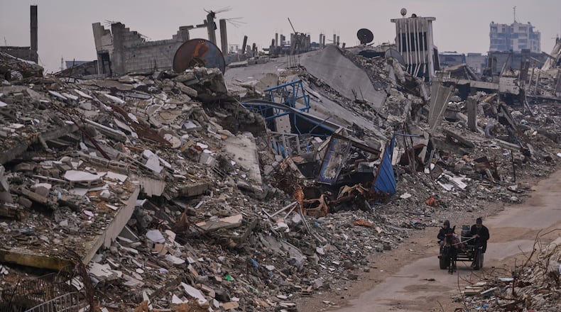 Palestinians pass along a street surrounded by buildings destroyed during Israeli air and ground operations in the Sheikh Radwan neighborhood, in Gaza City, Tuesday, Dec. 30, 2025. (AP Photo/Abdel Kareem Hana)