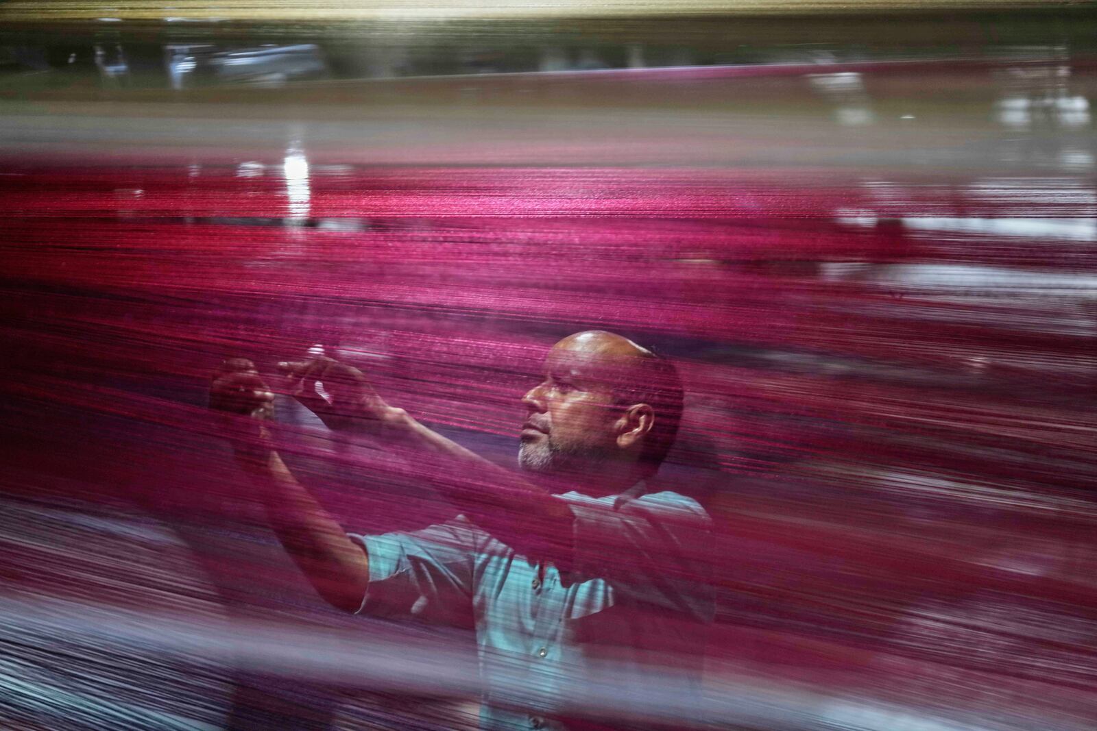 An Indian worker checks thread reels on a carpet weaving machine at a factory on the outskirts of Jammu, India, Tuesday, April 8, 2025. (AP Photo/Channi Anand)