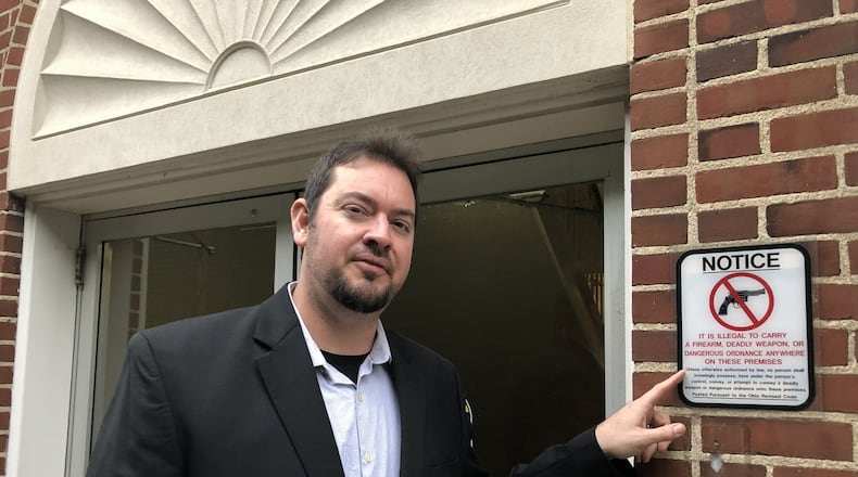 Lebanon City Councilman Joe Shafer points at one of the signs prohibiting the carrying of a firearm into city hall. In 2020, Shafer and other council members directed the law director to draft legislation to permit them to conceal-carry during meetings which was later adopted. STAFF FILE PHOTO
