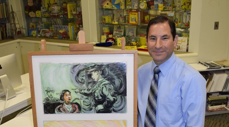 Curator of Exhibitions Jason Shaiman of Miami University Art Museum has his own collection of classic Curious George. He is pictured standing in his office with the collection of picture books and other Curious George memorabilia. CONTRIBUTED