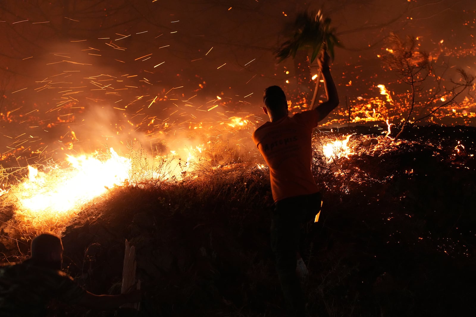 A man uses a branch to battle against a large wildfire burning in Kofinas, on the eastern Aegean island of Chios, Greece, late Sunday, June 22, 2025. (Pantelis Fykaris/Politischios.gr via AP)