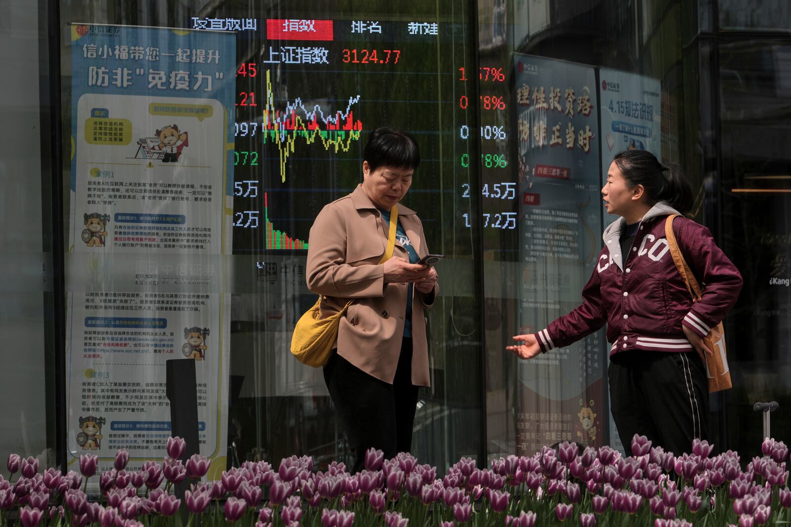Women talk near an electronic board displaying Shanghai shares trading index at a brokerage house, in Beijing, Tuesday, April 8, 2025. (AP Photo/Andy Wong)