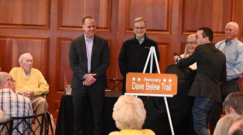 The Hamilton Community Foundation and the city of Hamilton honored Dave Belew, known by many as Mr. Hamilton, with a ceremony on Friday afternoon, May 10, 2024, that formally dedicated the portion of the Great Miami River Trail in the city with the honorary name the Dave Belew Trail. Belew, 92, at left, was the driving force behind getting the trail built in the city. Pictured is Jacob Stone-Welch, the Foundation's director of Donor Services, unveiling the sign that will be displayed at the various trail heads in Hamilton. MICHAEL D. PITMAN/STAFF