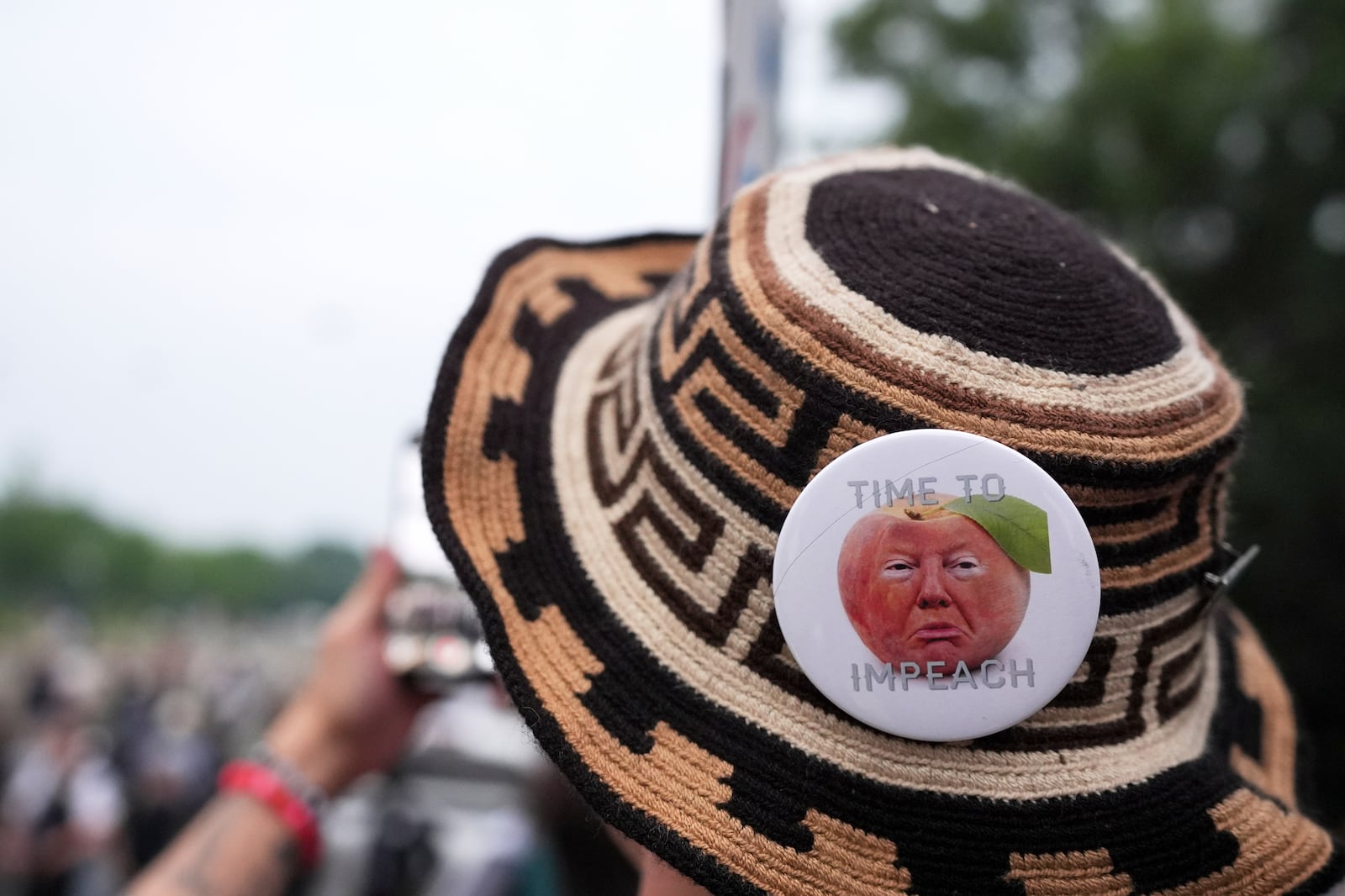 A demonstrator wears a pin stating "time to impeach" during a protest taking place on the day of a military parade commemorating the Army's 250th anniversary, coinciding with President Donald Trump's 79th birthday, Saturday, June 14, 2025, in Washington. (AP Photo/Evan Vucci)