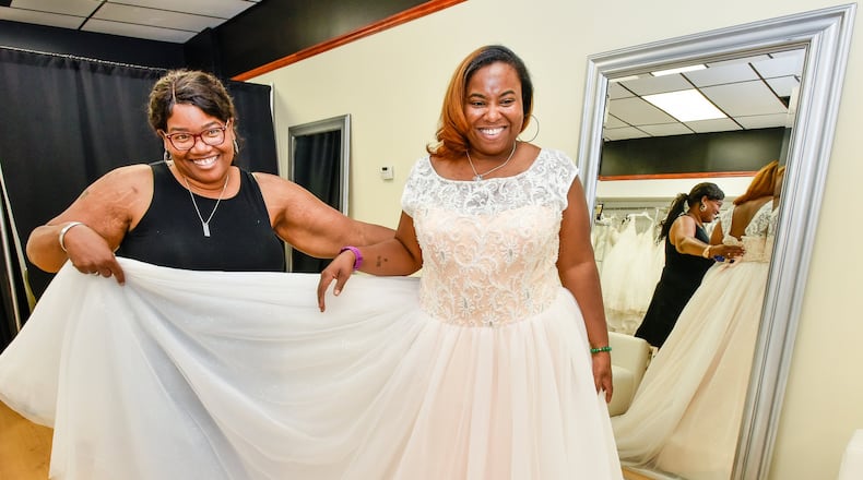 Owner Jonda Prather, left, holds a dress for Jennifer Norman as they finalize looks for a wedding themed photo shoot Wednesday, June 26 at Belle Bridal Boutique on Central Avenue in Middletown. Prather says her shop specializes on plus size bridal gowns. NICK GRAHAM/STAFF