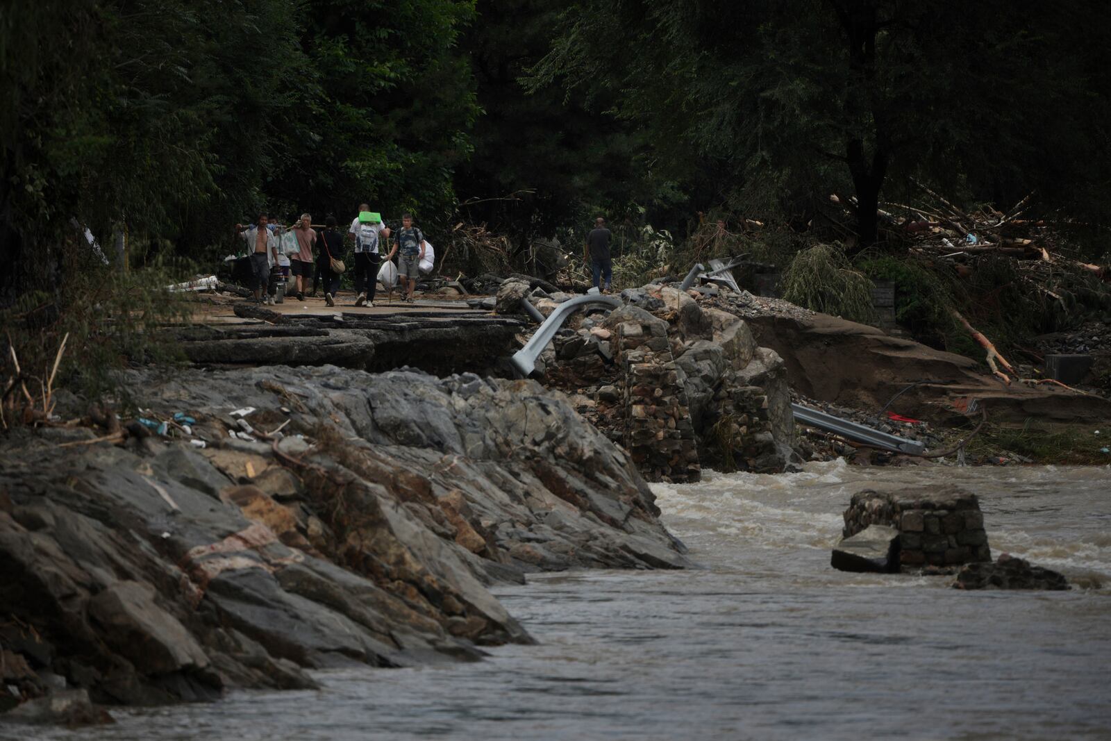 Villagers carrying belonging walk on a road damaged by flood as they evacuate from the Langjiayu village after heavy rains in Miyun district on the outskirts of Beijing, Tuesday, July 29, 2025. (AP Photo/Andy Wong)