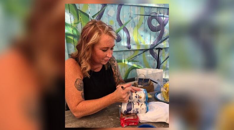 Nicki Tate, who designed the Falconer's Flight beer can, signs some of them Monday night during a soft launch party at New Ales Brewery in Middletown. CONTRIBUTED