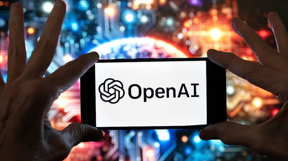 FILE - The OpenAI logo is seen displayed on a cell phone in front of an image on a computer screen generated by ChatGPT's Dall-E text-to-image model, Friday, Dec. 8, 2023, in Boston. (AP Photo/Michael Dwyer, file)