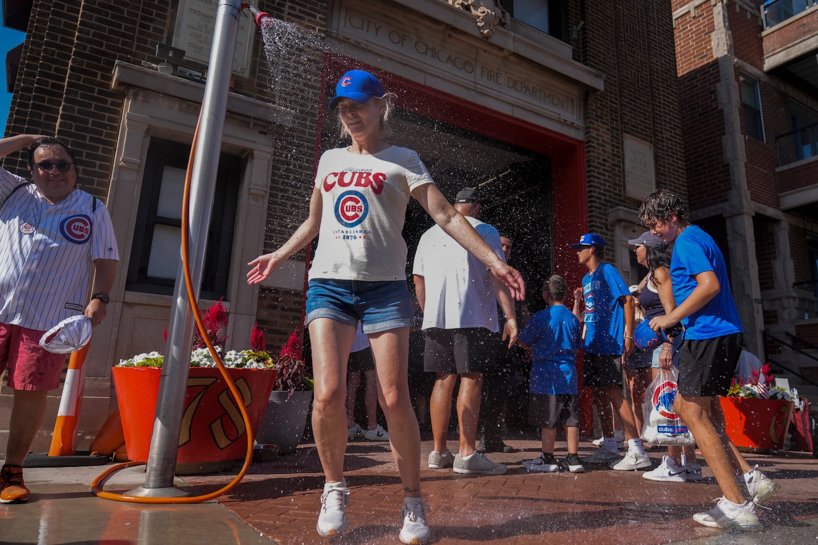 Baseball fans cool off under a sprinkler provided by the Chicago Fire Department outside of Wrigley Field after a hot baseball game between the Seattle Mariners and Chicago Cubs, Saturday, June 21, 2025, in Chicago. (AP Photo/Erin Hooley)
