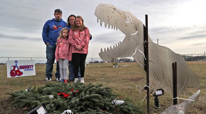 Barrett Fitzsimmons' parents Brad and Lana along with his sisters  Brayden and Braelynn look over Barrett's grave at Myers Cemetery in Pike Township Thursday. Two years after Barrett died at the age of 9-years-old from cancer the family is still not permitted to place a permanent headstone on his grave because of a disagreement with the cemetery trustees over the design.  A metal cutout of a dinosaur, which Barrett loved, is the only thing that marks the grave. BILL LACKEY/STAFF