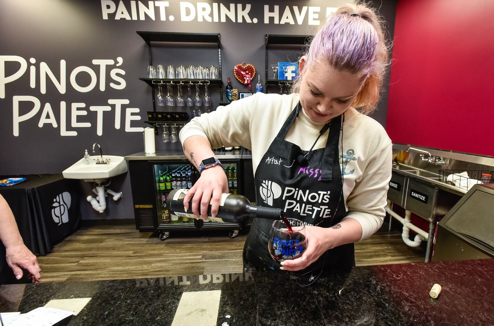 Missy Baker, assistant manager and artist at Pinot’s Palette, pours a glass of wine during an event at the Pinot’s Palette location on Tylers Corner in West Chester Township Monday, April 8, 2019. The business is a place to gather with friends with a glass of wine or beer while a local artist guides you through painting your own piece of art on a canvas. NICK GRAHAM/STAFF