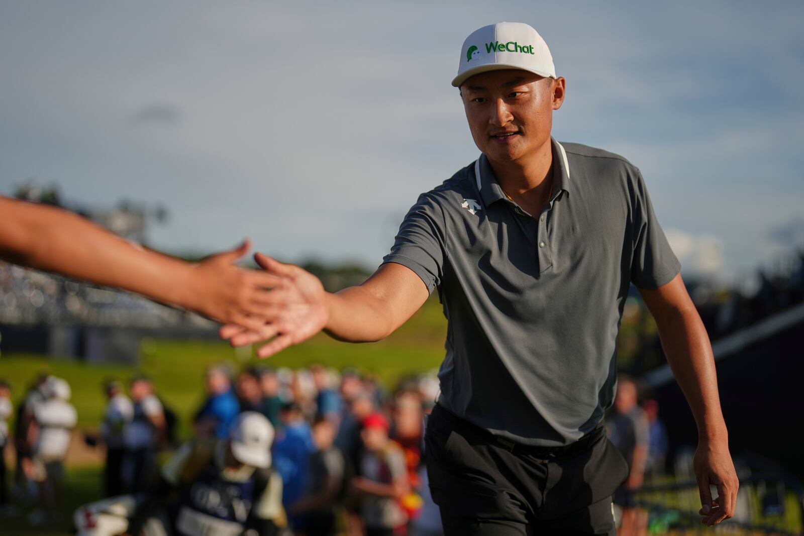 Li Haotong of China taps hands with members of the public as he walks to the 18th tee during the third round of the British Open golf championship at the Royal Portrush Golf Club, Northern Ireland, Saturday, July 19, 2025. (AP Photo/Francisco Seco)