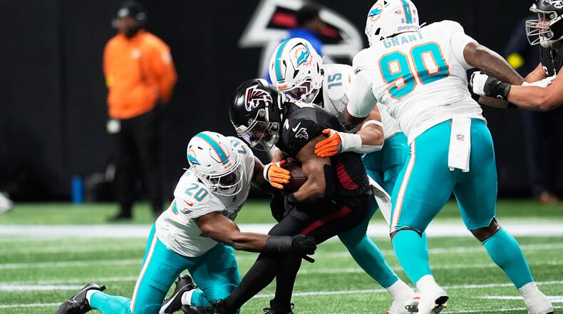 Miami Dolphins linebacker Jordyn Brooks (20) and linebacker Jaelan Phillips (15) defend Atlanta Falcons running back Bijan Robinson, center, during the first half of an NFL football game, Sunday, Oct. 26, 2025, in Atlanta. (AP Photo/Mike Stewart)
