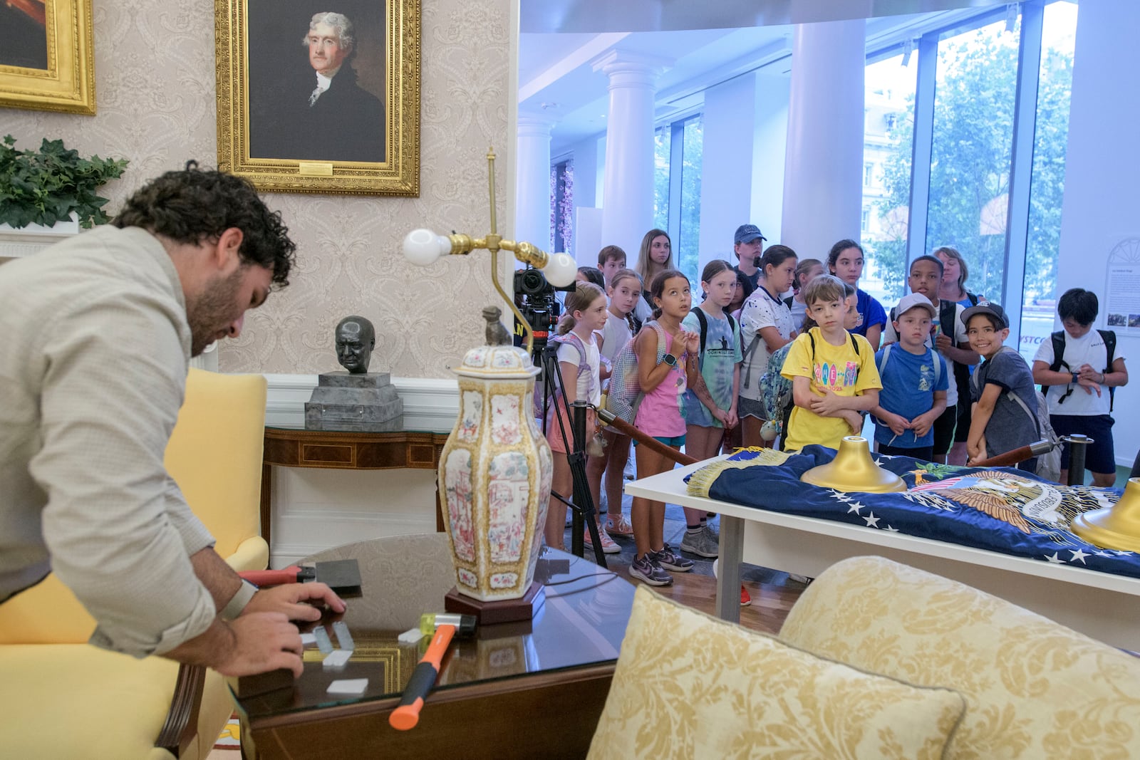 While a group of children look on, Luke Boorady works with a lamp during work to transition a replica of the White House Oval Office from the days of former President Joe Biden with President Donald Trump's decor, at the White House Historical Association in Washington, Wednesday, July 23, 2025. (AP Photo/Rod Lamkey, Jr.)