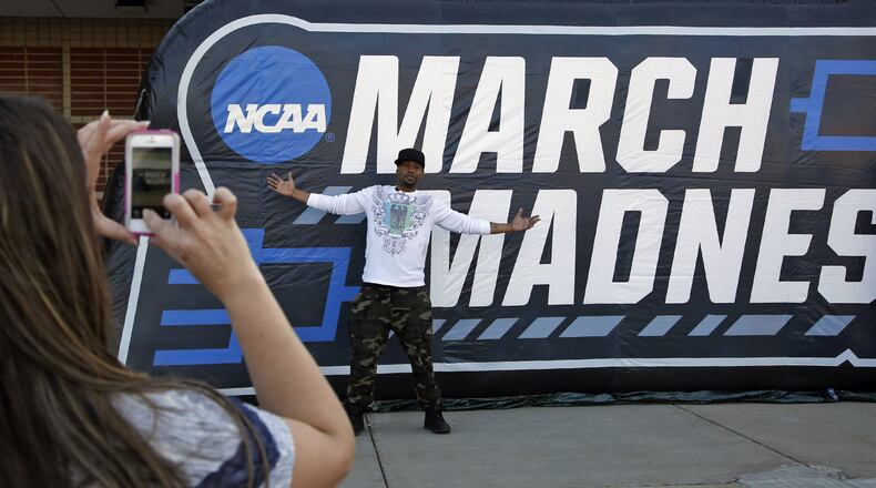 Christy Flint photographs Mac Heath with the March Madness sign before the NCAA First Four games began. TY GREENLEES / STAFF