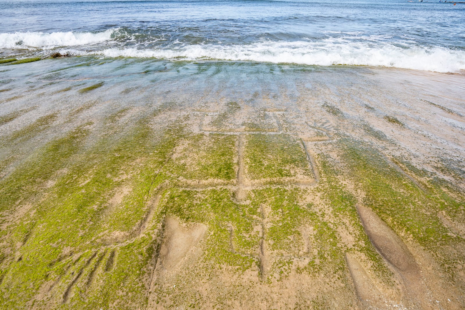Ancient petroglyphs carved as human figures are visible on the exposed rock surface at Pokai Bay, July 22, 2025, in Waianae, Hawaii. (AP Photo/Mengshin Lin)