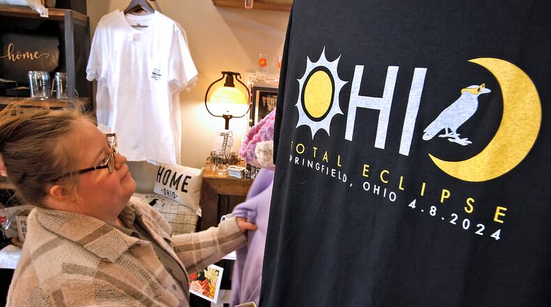 Jordan Lyons straightens a display at Champion City Guide and Supply Wednesday, March 20, 2024. The new total eclipse t-shirts, on sale at the downtown Springfield store, have quickly become very popular. BILL LACKEY/STAFF