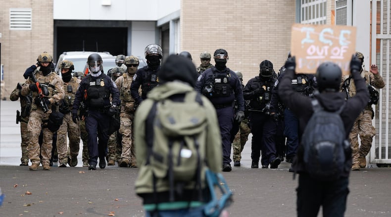 FILE - People protest outside a U.S. Immigration and Customs Enforcement facility as law enforcement officers walk out of the gates to guard vehicles leaving the facility on Oct. 11, 2025, in Portland, Ore. (AP Photo/Jenny Kane, File)