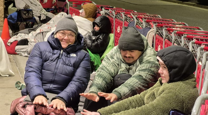 Joy Stott, Elijah Babin and London Huling used a portable heater to stay warm while waiting overnight at the Beavercreek Target store for Black Friday giveaways. The first 100 customers got a tote bag filled with gifts. MICHAEL KURTZ / STAFF