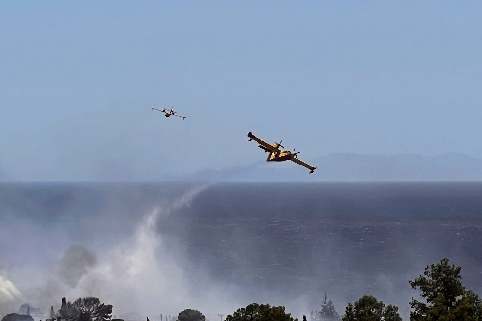 Firefighting planes drop water while battling a blaze in the seaside area of Palaia Fokaia, south of Athens, Thursday, June 26, 2025, as authorities evacuate five locations during Greece's first summer heatwave with temperatures nearing 40 degrees Celsius (104 Fahrenheit).(AP Photo/Giorgos Delveroudis)