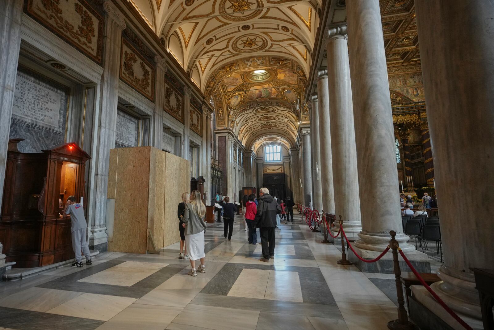 People walk past a wooden board where work in progress is taking place on the spot where Pope Francis will be buried, inside St. Mary Major basilica, in Rome, Tuesday, April 22, 2025. (AP Photo/Alessandra Tarantino)