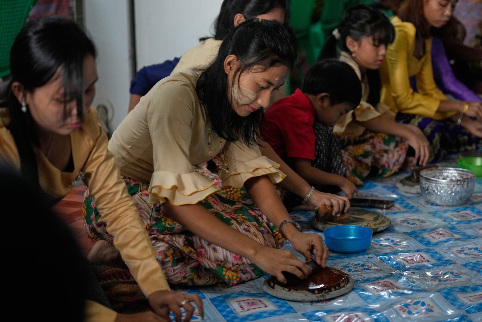 Myanmar's Rakhine ethnic women make sandalwood liquid to make fragrant water as they prepare to doze the fragrant water on Buddha images during the first day of annual traditional water festival also known as "Thingyan", in Yangon, Myanmar, Sunday, April 13, 2025. (AP Photo/Thein Zaw)