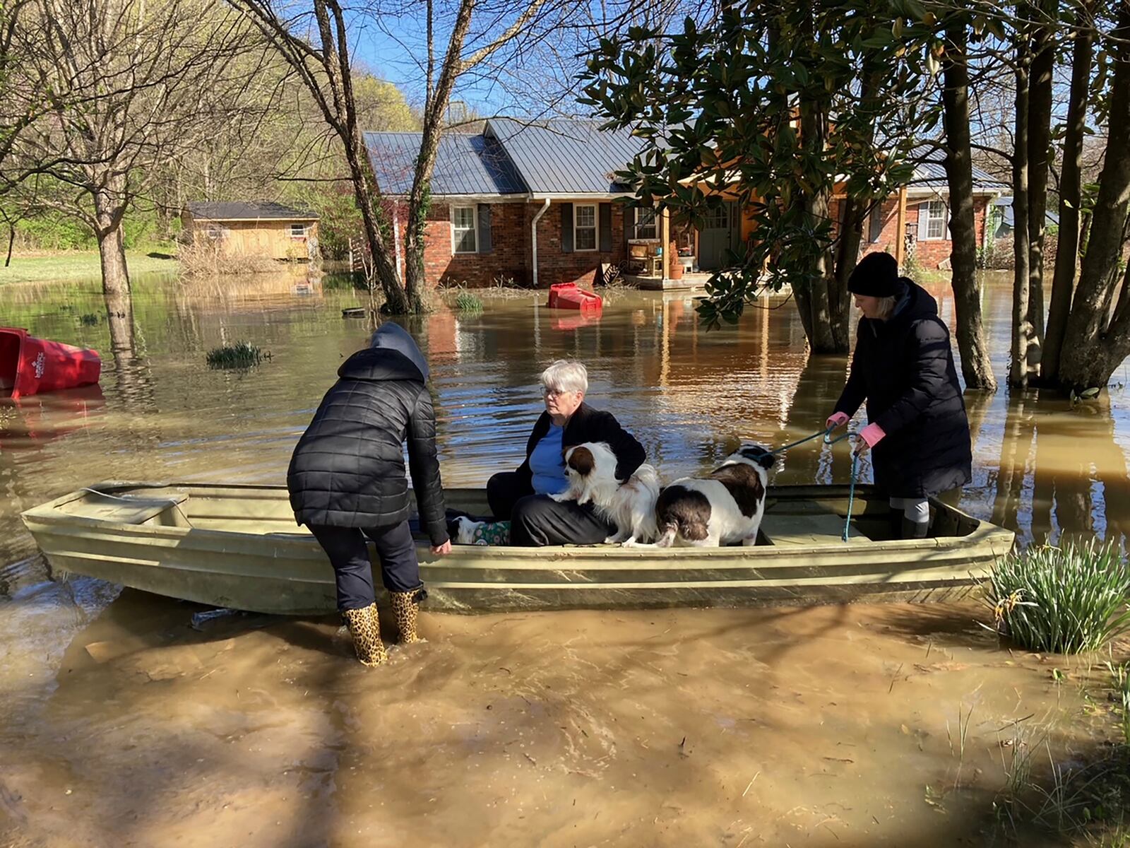 Susan Williams sits in a boat with her dogs as they prepare to return home amid floodwaters on Tuesday, April 8, 2025 near Frankfort, Ky. Two of her friends helped Williams make the short boat ride back to her home. (AP Photo/Bruce Schreiner)