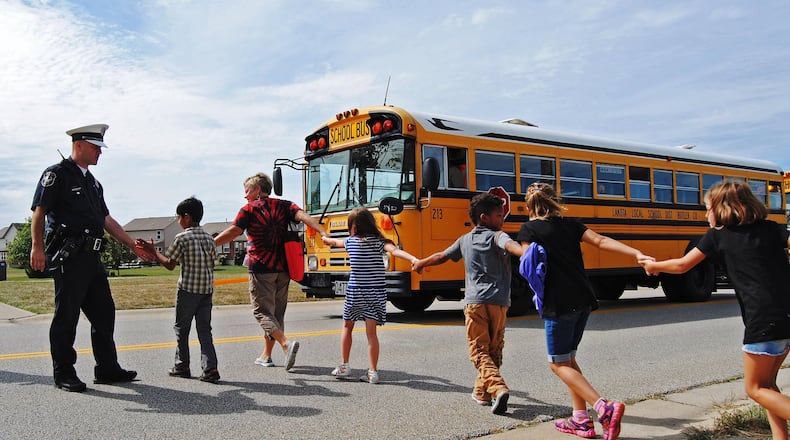 A West Chester Twp. police officer gives high-fives to Endeavor Elementary students as they board a bus to be transported to Lakota West Freshman School after a bomb threat forced the school to be evacuated in 2015. ERIC SCHWARTZBERG/STAFF
