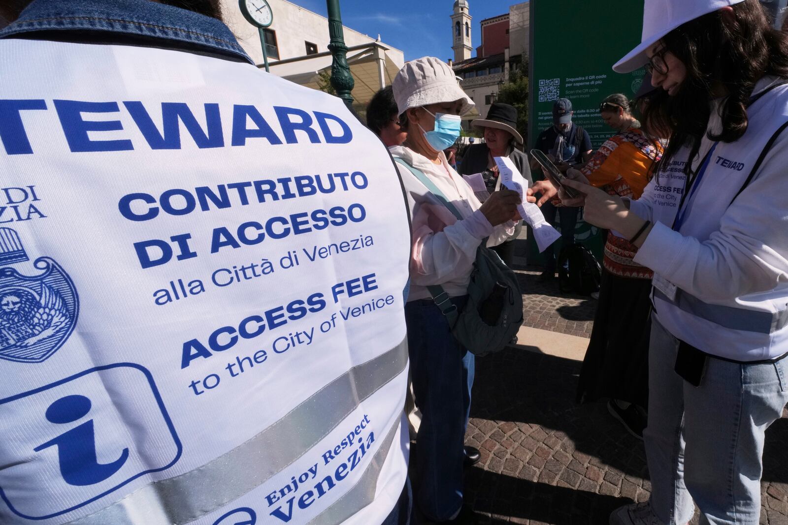 Stewards check tourists' QR codes outside the main train station in Venice, Italy, Friday, April 18, 2025, as the city for a second year is charging day-trippers an arrivals tax. (AP Photo/Antonio Calanni)