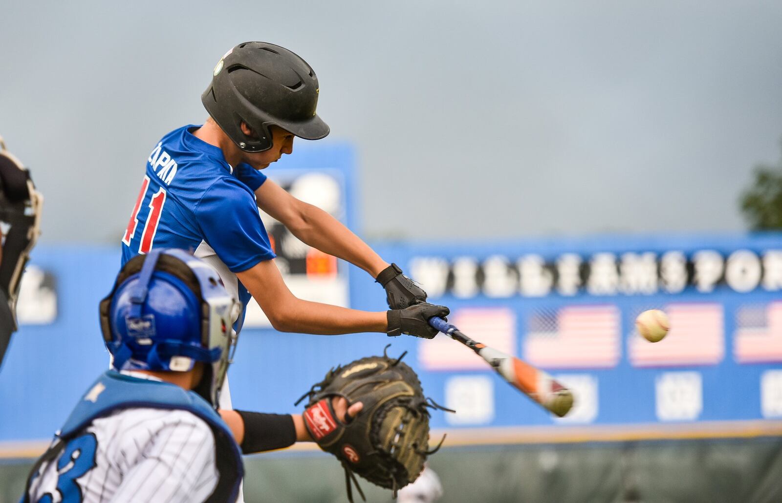 Hamilton-Fairfield’s Jordan Zapata connects at the plate in front of Hamilton West Side catcher Peyton Eldridge (13) during Tuesday night’s winners’ bracket final of the Little League District 9 tournament. Host West Side won 10-0. NICK GRAHAM/STAFF