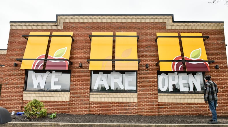 Jarett Trudel, general manager of Applebee’s in Hamilton, paints “We Are Open” on the side windows Tuesday, March 31 as a way to let people know they are still serving food. They are open 11 a.m. to 9 p.m. with for carryout orders by phone or web ordering. NICK GRAHAM / STAFF