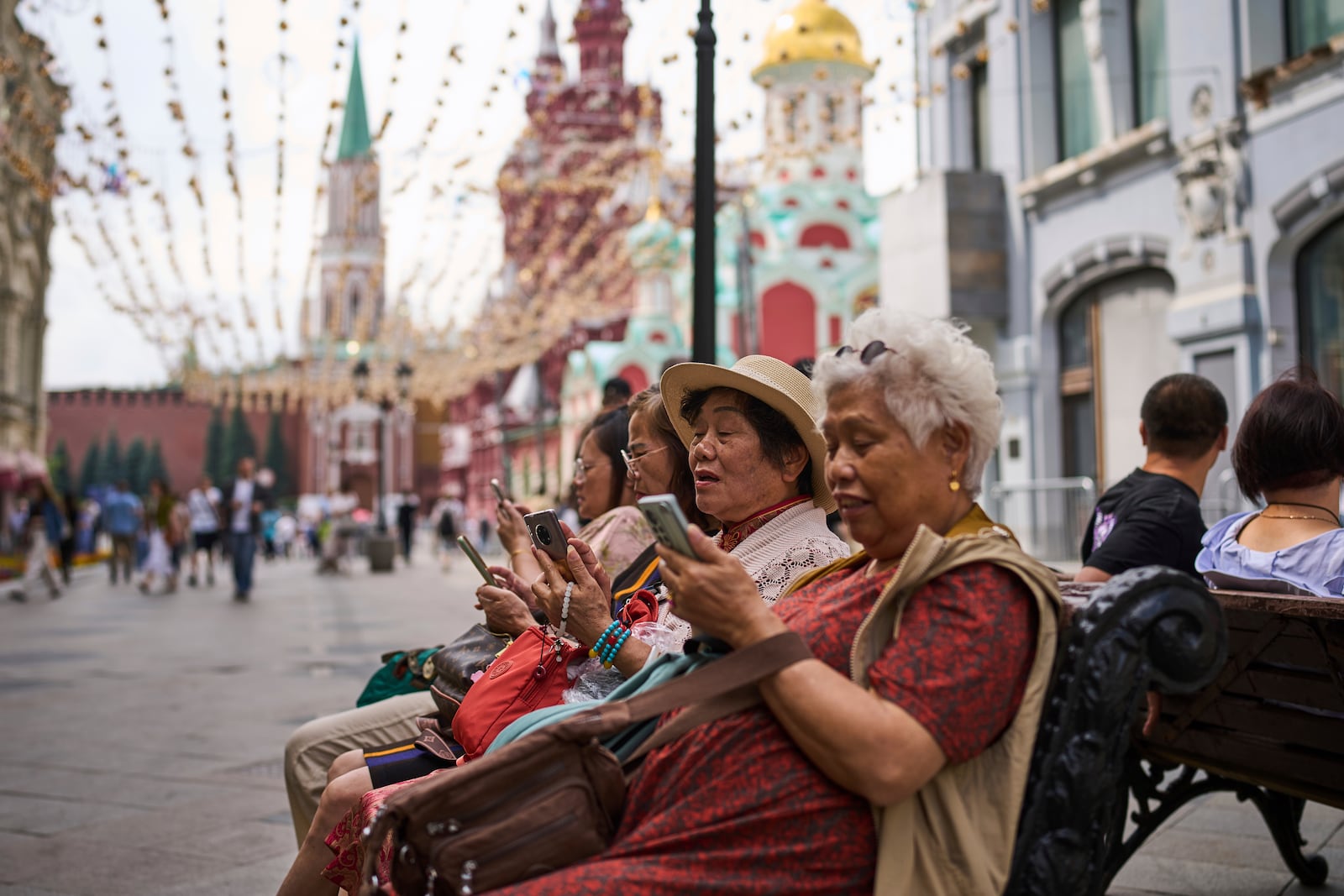 Tourists sitting near the Kremlin in Moscow look at their phones on Wednesday, July 16, 2025. (AP Photo/Alexander Zemlianichenko)