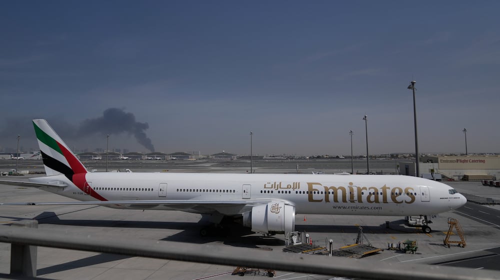ADDS CAUSE OF BLACK SMOKE IN THE BACKGROUND.- A plume of smoke caused by an Iranian strike is seen in the background an an Emirates plane is parked at the Dubai International Airport after its closure in Dubai, United Arab Emirates, Sunday, March 1, 2026. (AP Photo/Altaf Qadri)