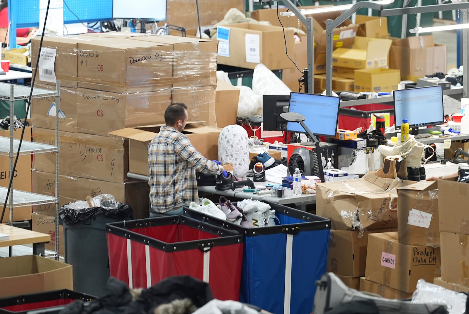 A man works amid boxes of returned or overstocked clothing, shoes, boots, coats, packs and other items in a warehouse where the goods are cleaned or repaired before they are marketed on resale platforms in Englewood, Colo., on Thursday, April 17, 2025. (AP Photo/David Zalubowski)