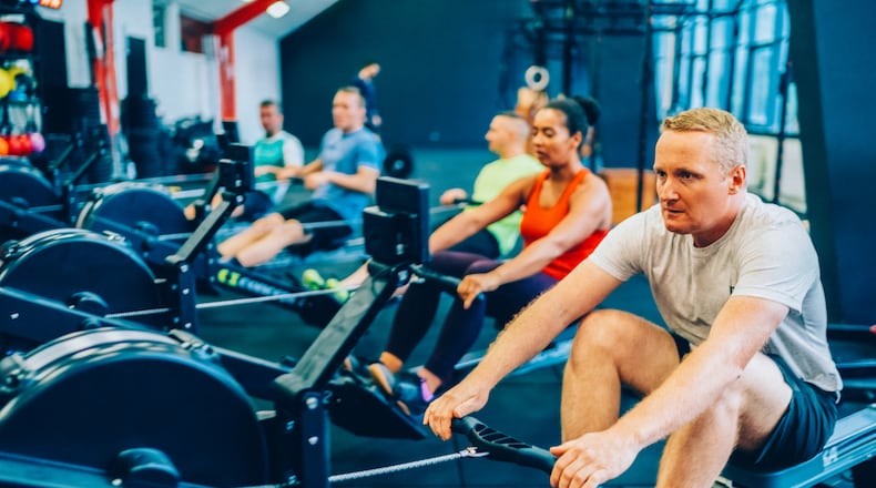 A group of individuals work out together on indoor rowing machines in a modern gym. ISTOCK