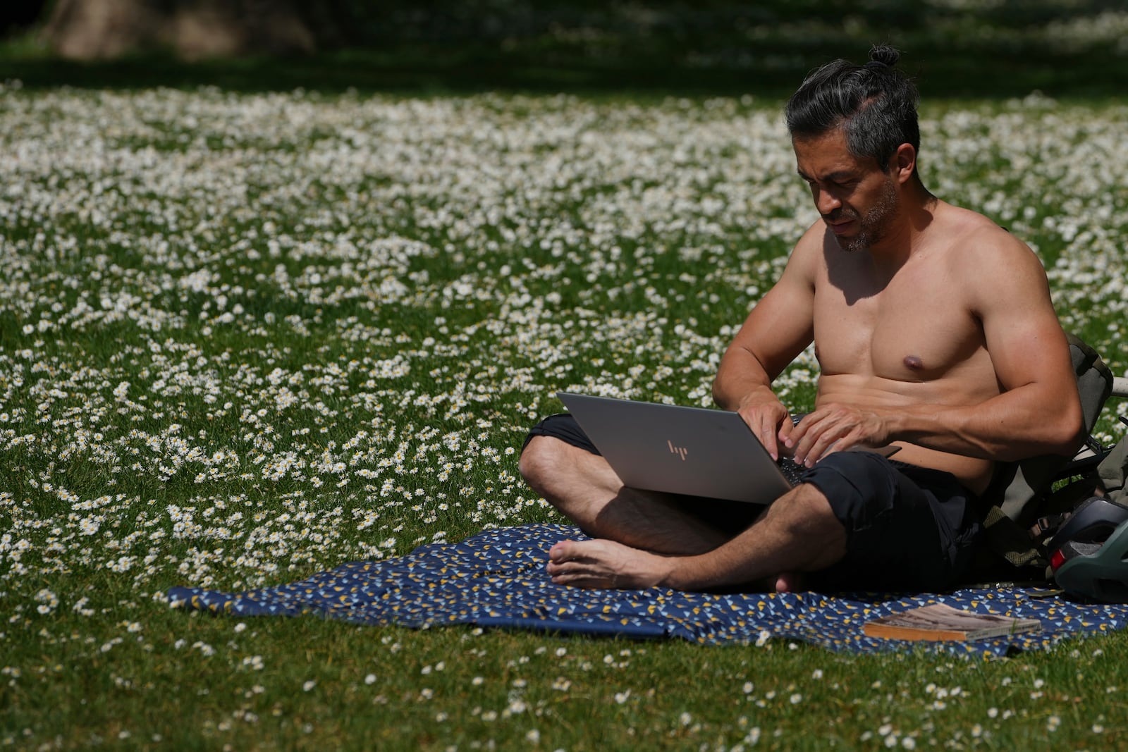 A man uses his computer on a sunny day at a park in London, Wednesday, April 30, 2025. (AP Photo/Kin Cheung)