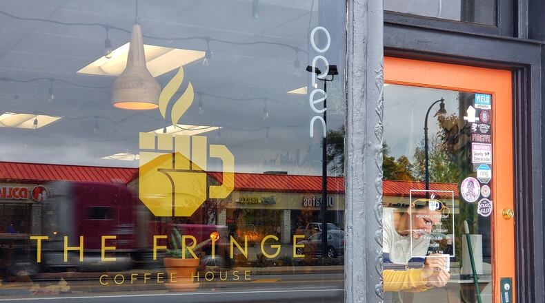 Ashley Ingle installs hours signage to the front door of The Fringe Coffee House, which is scheduled to open Thursday, Oct. 29, 2020 in Hamilton. NICK GRAHAM / STAFF