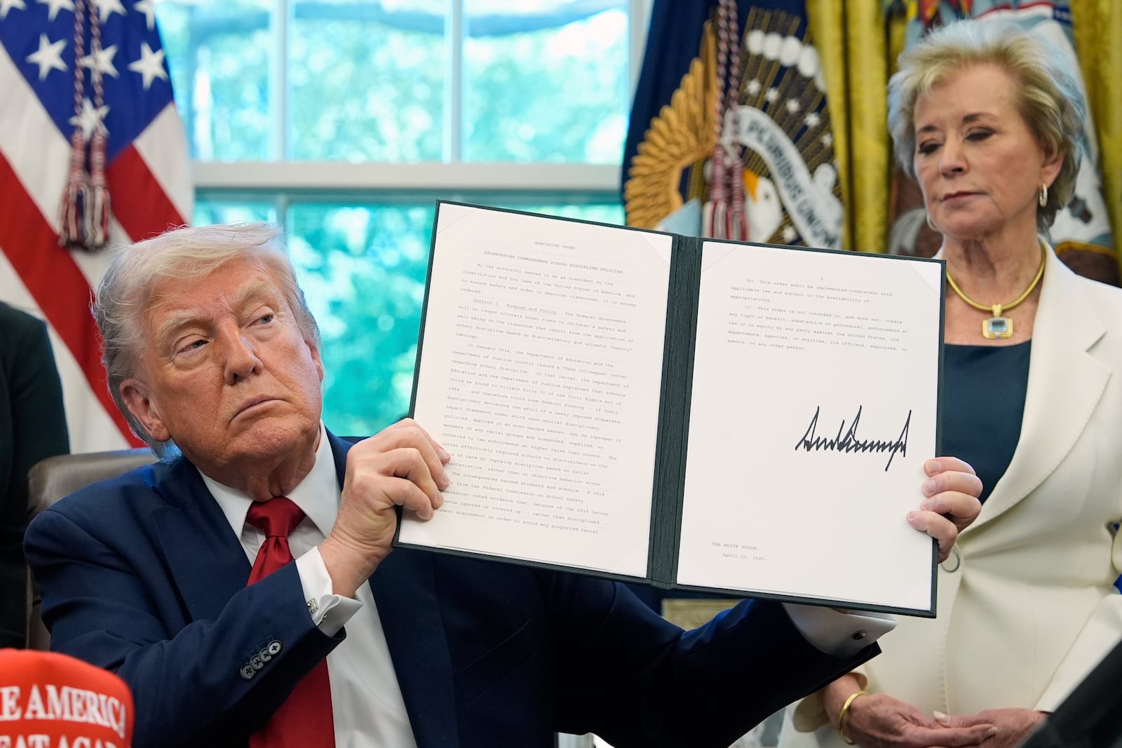 FILE - President Donald Trump holds a signed an executive order relating to school discipline policies as Education Secretary Linda McMahon listens in the Oval Office of the White House, April 23, 2025, in Washington. (AP Photo/Alex Brandon, file)