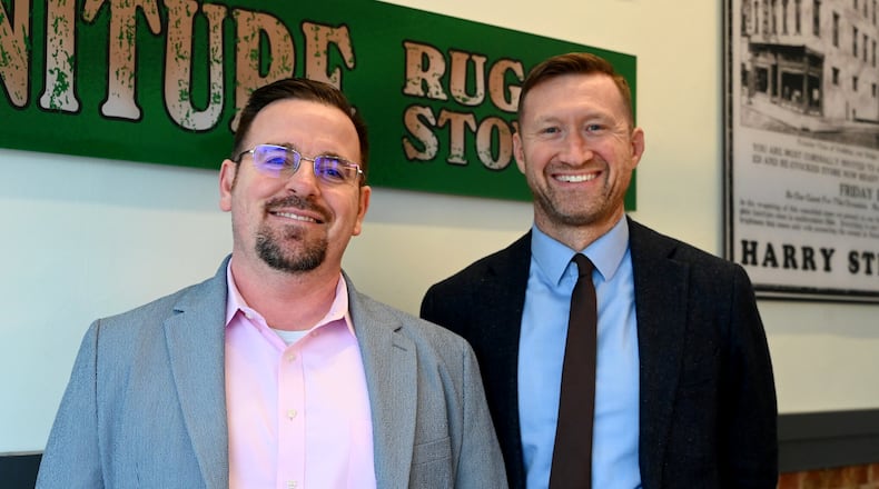 Josh Hodges (left) and Scott Kruger stand inside their new law office, Kruger & Hodges at the corner of South Third and Ludlow streets on Nov. 24, 2025, in Hamilton. During renovation, they uncovered what may be the original glass to the 19th-century building. The glass was painted advertising a former furniture store, but they couldn't remove it without breaking it. Hodges and Kruger had replicated the painted glass and it's on display in the office. MICHAEL D. PITMAN/STAFF