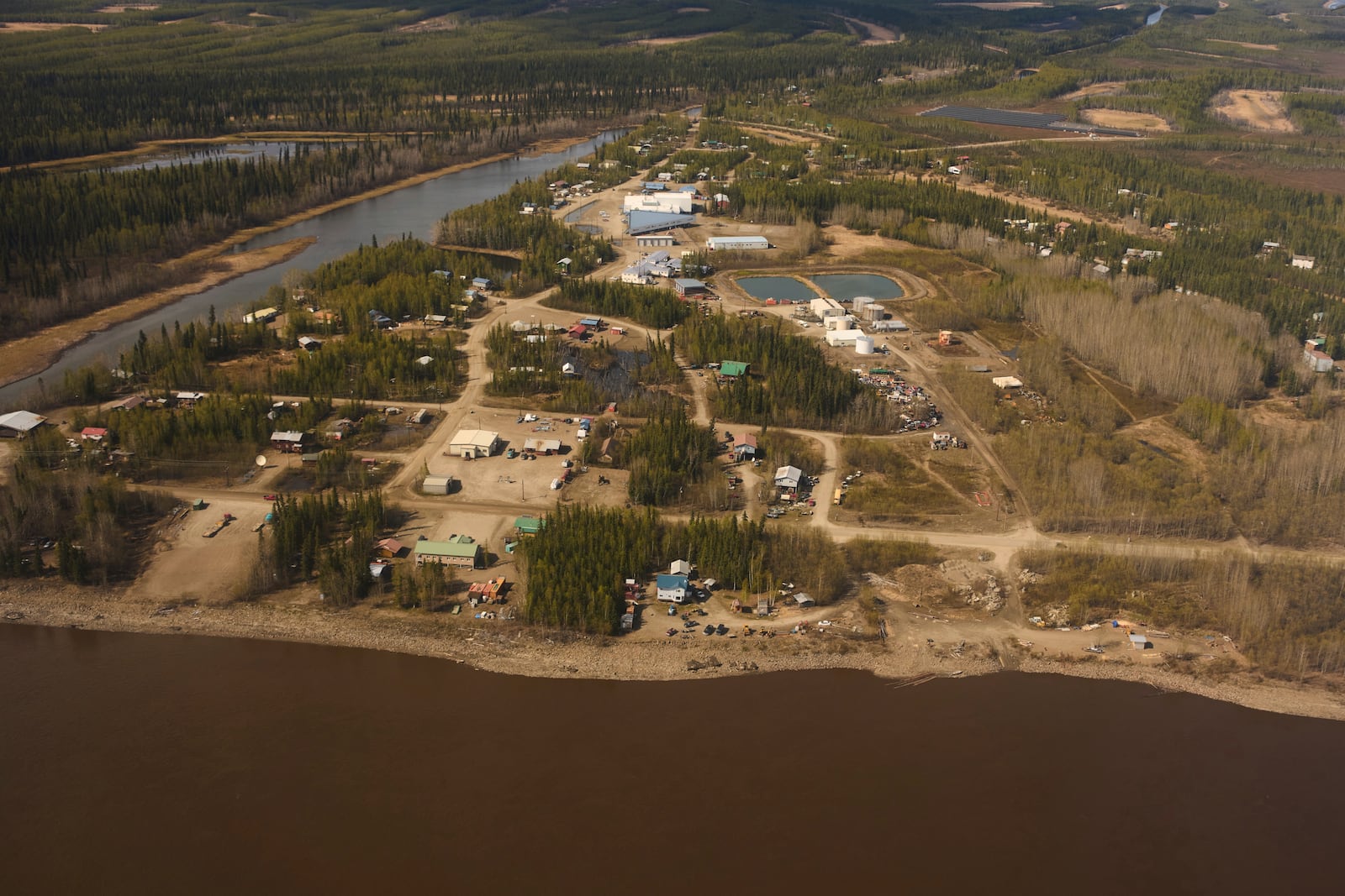 Buildings line dirt roads near the Yukon River, front, Friday, May 23, 2025, in Galena, Alaska. (AP Photo/John Locher)