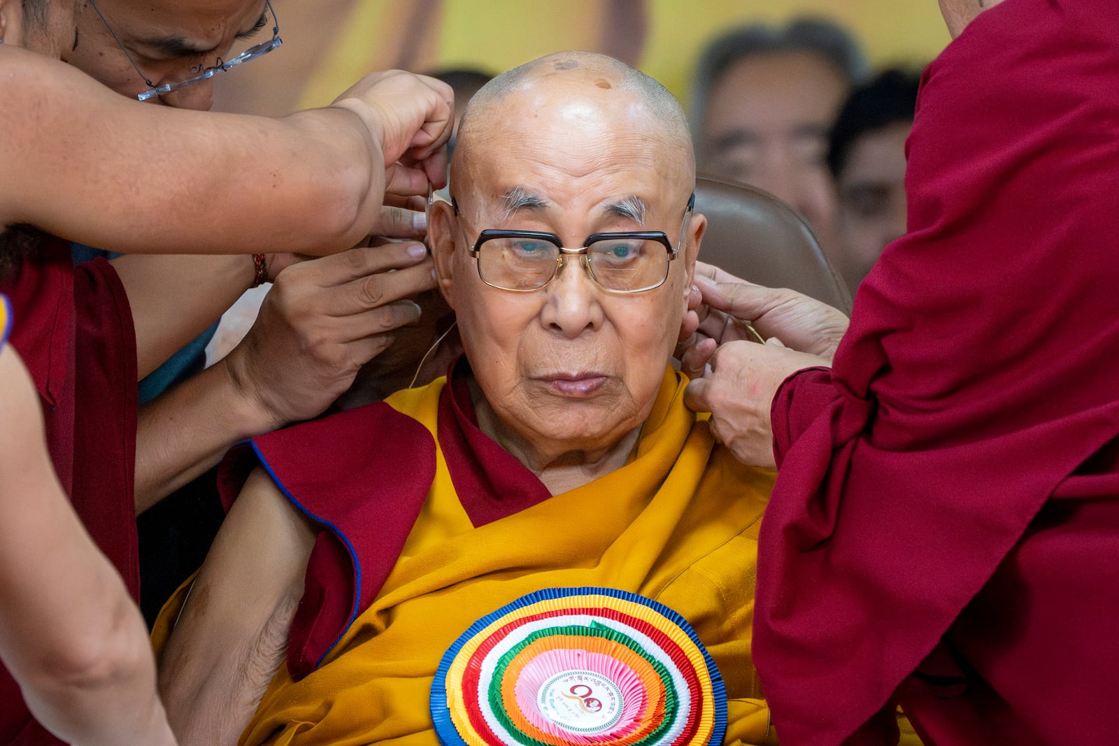 Attendant monks help put a microphone around Tibetan spiritual leader the Dalai Lama's head during his 90th birthday celebrations at the Tsuglakhang temple in Dharamshala, India, Sunday, July 6, 2025.(AP Photo/Ashwini Bhatia)