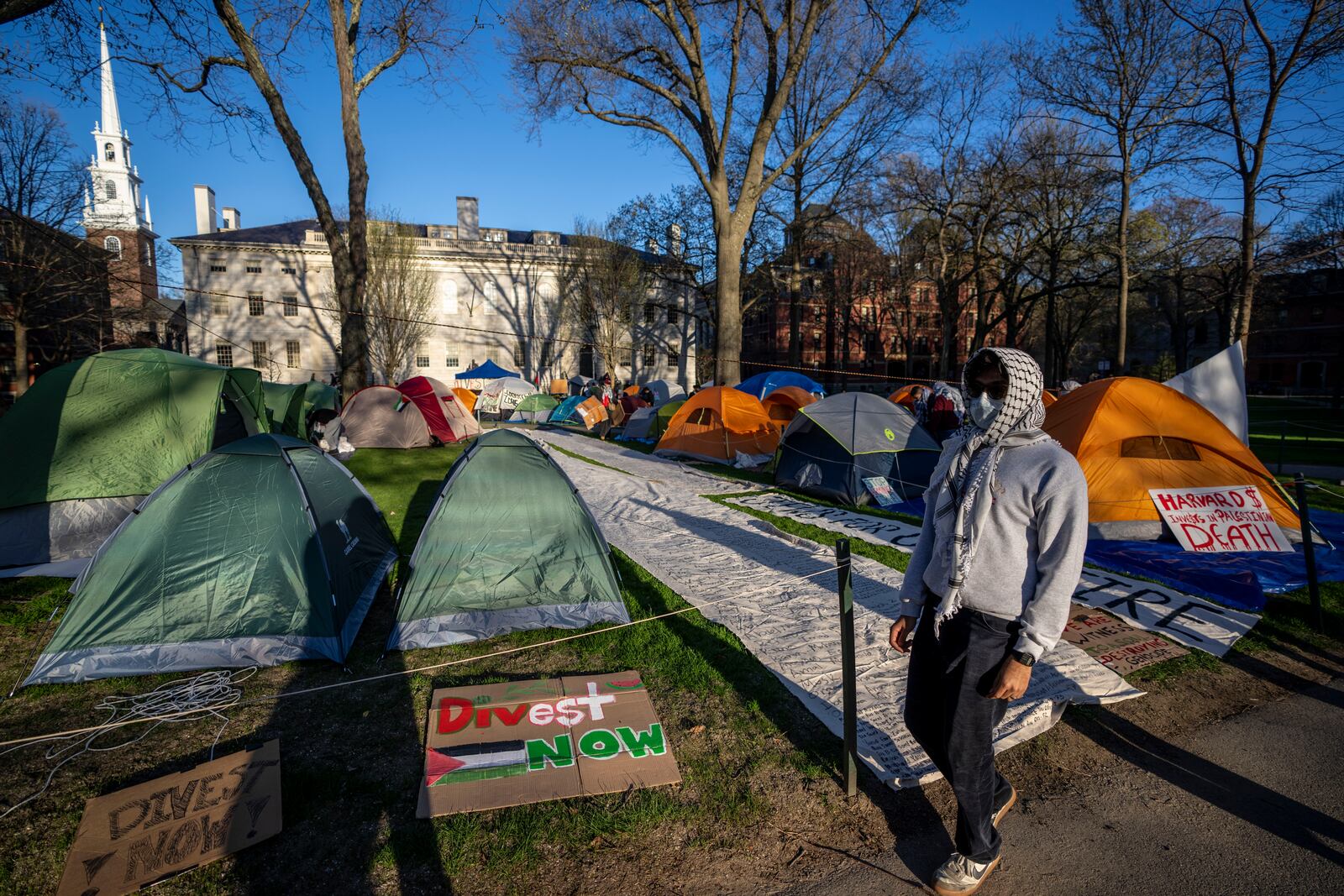 FILE - A student protester against the war in Gaza walks past tents and banners in an encampment in Harvard Yard, at Harvard University in Cambridge, Mass., on April 25, 2024. (AP Photo/Ben Curtis, file)