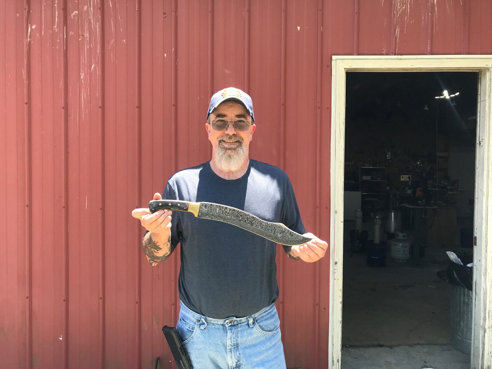 Bill Pyles, the Forged in Fire Champion, stands outside his forging workshop with the blade he constructed for the first challenge. The blade was constructed with 160 sheets of steel, fire hose and bunker gear.
