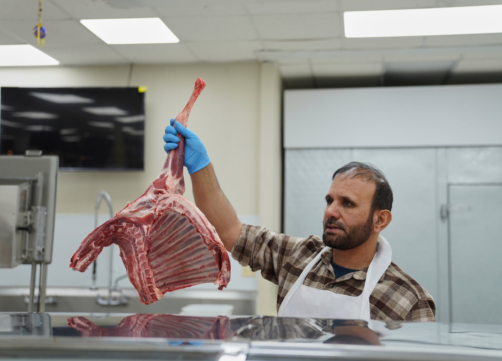Shahpoor Essazada, a butcher at the Finest Supermarket halal grocery store in Fredericksburg, Va., holds up a piece of meat for a customer, on Monday, April 7, 2025. (AP Photo/Jessie Wardarski)