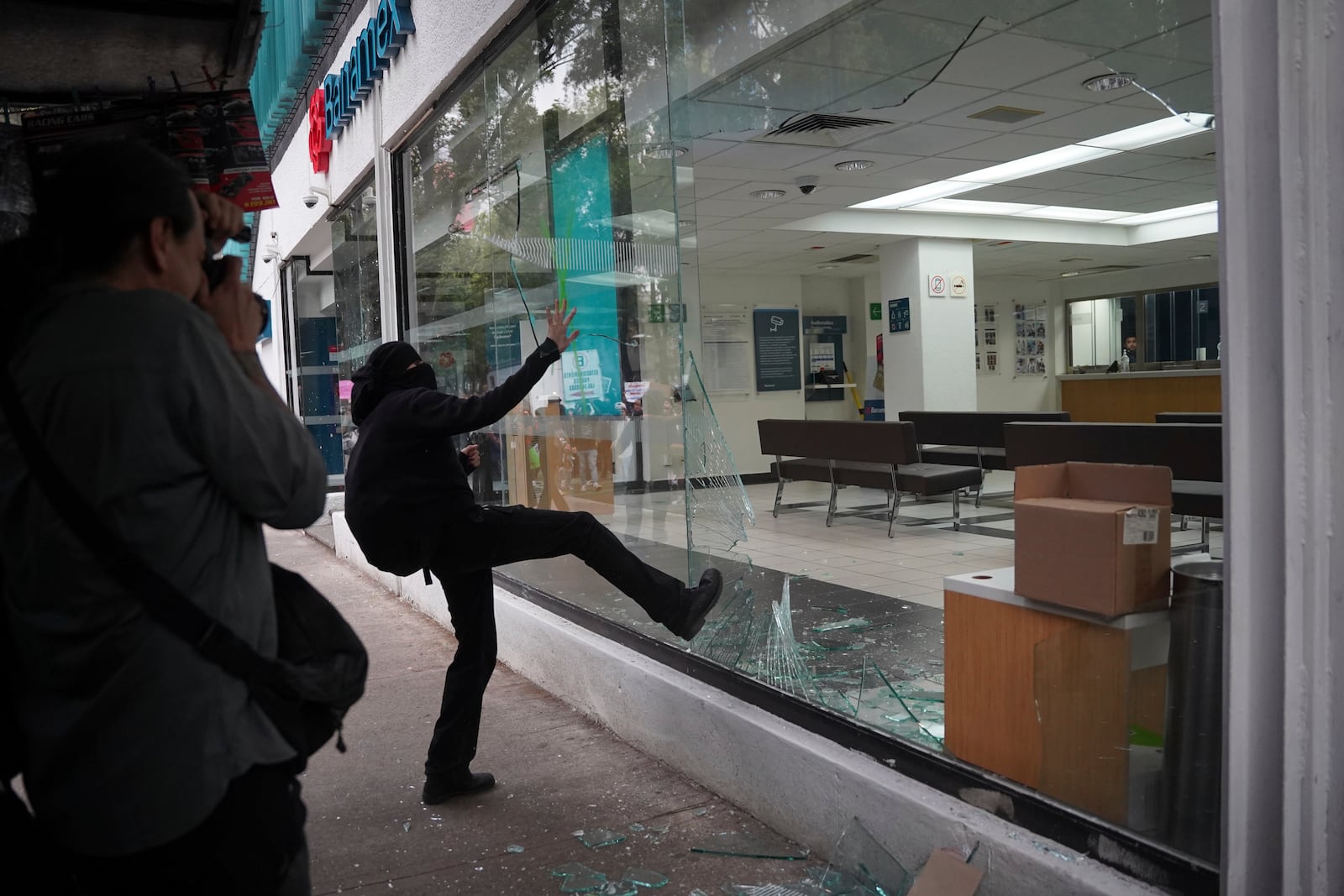 A demonstrator kicks in a bank storefront window at the end of peaceful protest that turned violent against gentrification, as the increase in remote workers has risen prices and increased housing demand in neighborhoods like Condesa and Roma, in Mexico City, Friday, July 4, 2025. (AP Photo/Aurea Del Rosario)