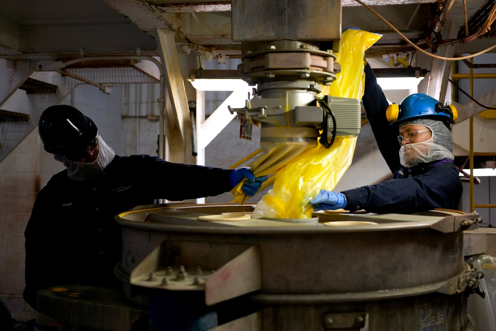 Jobe Washington, right, and Dwight Brown use a large sifter to mix a shade of yellow coloring at Sensient Technologies Corp., a color additive manufacturing company, in St. Louis, on Wednesday, April 2, 2025. (AP Photo/Jeff Roberson)