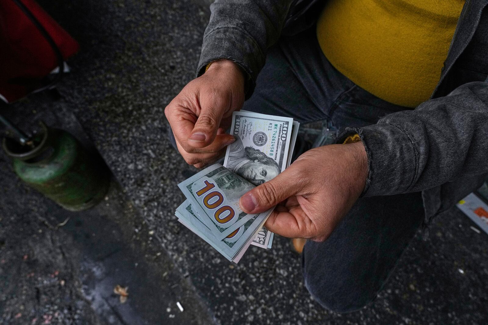 A street money exchanger poses for a photo without showing his face as he counts U.S. dollars at Ferdowsi square, Tehran's go-to venue for foreign currency exchange, in downtown Tehran, Iran, Saturday, April 5, 2025. (AP Photo/Vahid Salemi)